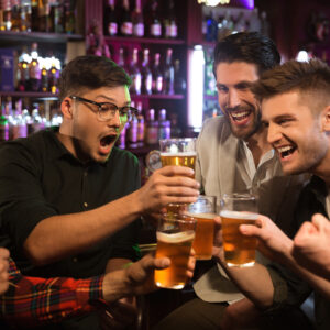 Happy smiling male friends clinking with beer mugs in pub